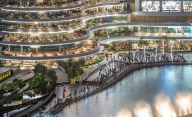 Shopping mall balcony with reataurants near fountain in Dubai downtown aerial night timelapse, United Arab Emirates. Illuminated waterfront walking area